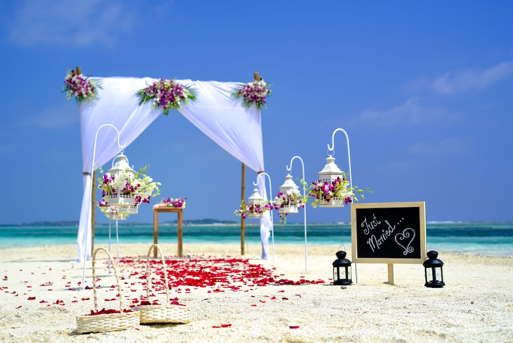 A beach-wedding setting with rose petals on the sand 