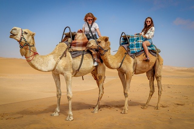 Two women riding camels in the desert