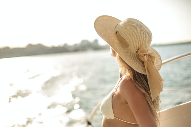 A woman in a bikini with a white hat on a yacht 