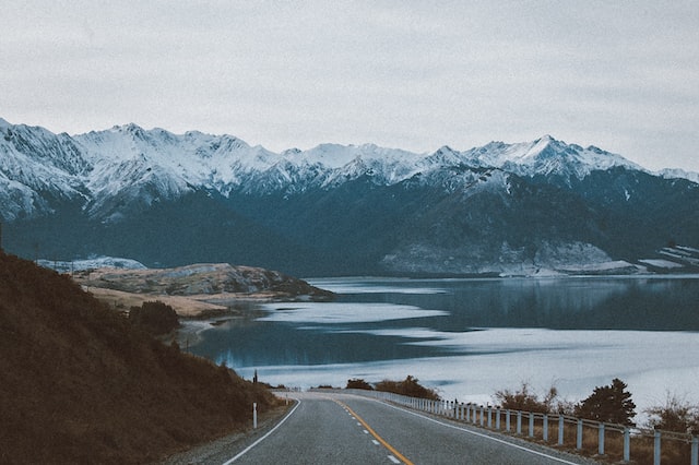 A road next to a lake and mountains that is a natural scenic drive through Alaska.