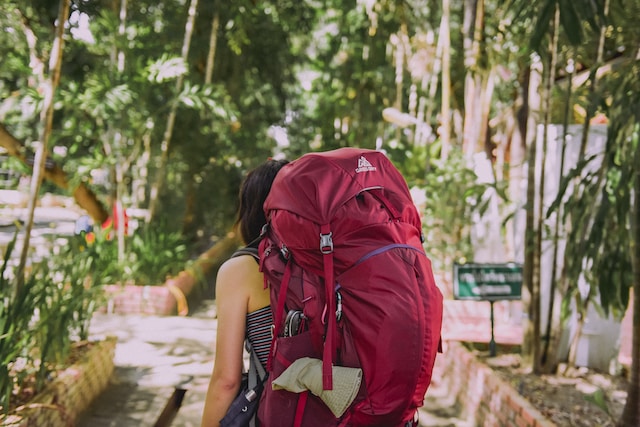 a girl with red backpack walking down a trail shows why you need to try solo travel